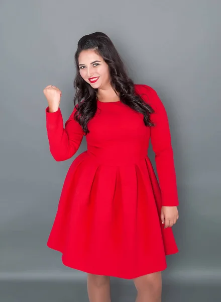 プラスサイズの女性はいジェスチャーを示す灰色の背景に赤のドレスで幸せ — ストック写真