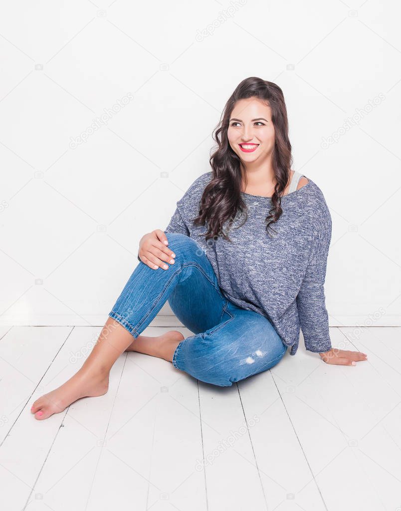 Beautiful happy plus size woman barefoot sitting on the floor. Body positive concept