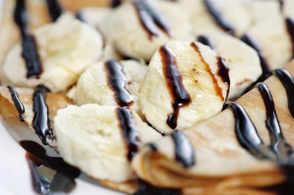 バナナとチョコレートの白い背景がある薄いおいしいパンケーキ — ストック写真