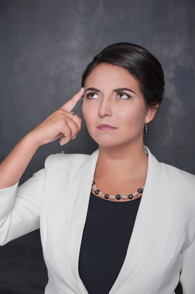 Beautiful woman with finger to her head on blackboard background — Stock Photo, Image