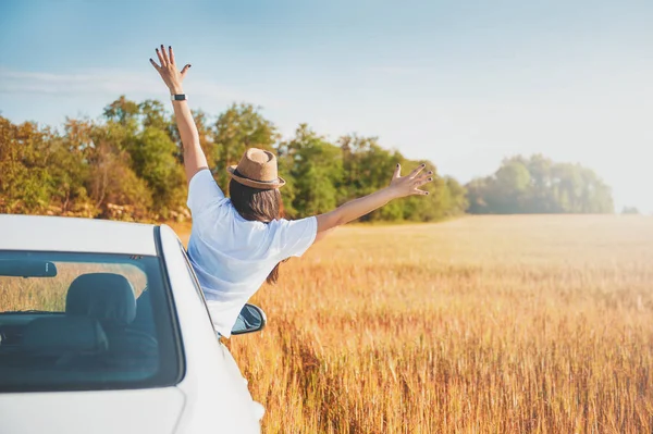 Young woman with hands raised in white car on the field