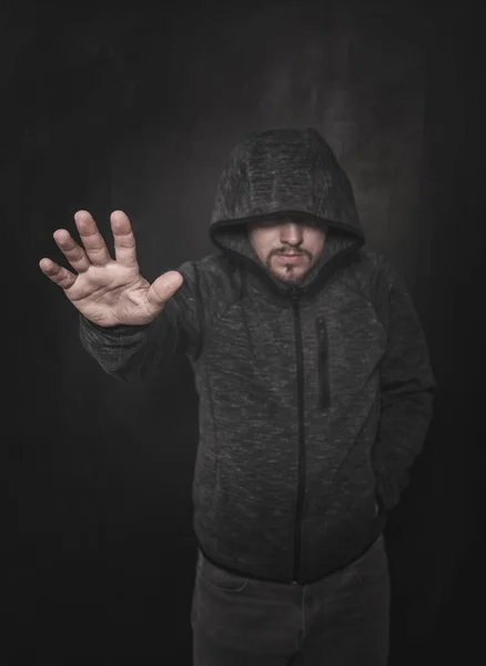 Unknown man in hood pointing by hand on dark. Focus on hand