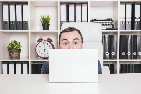 Scared business man hiding behind laptop