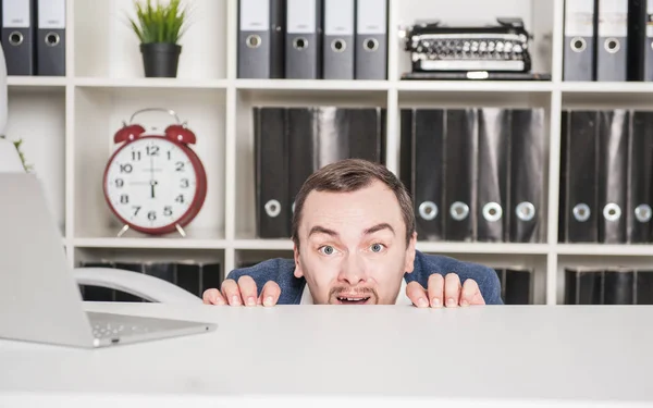 Scared business man hiding behind the table — Stock Photo, Image