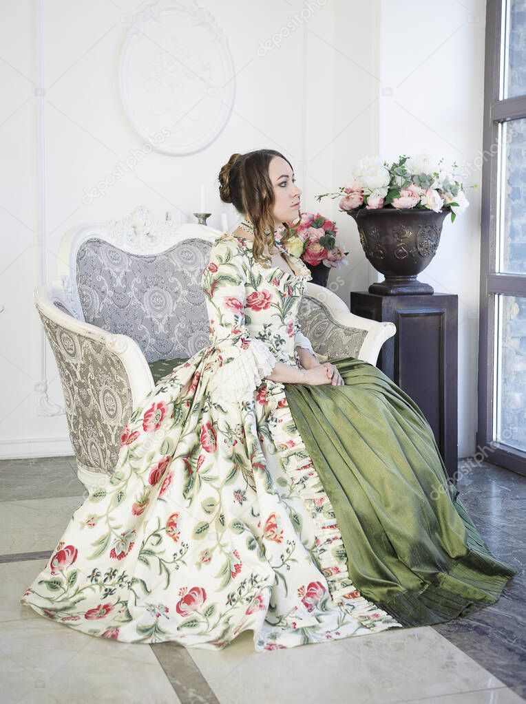 Beautiful woman in long green medieval dress sitting near window