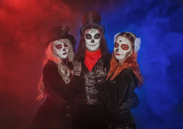 不気味なハロウィンを持つ3人の美しいグループは 赤と青の煙の背景に死んだ日カラベラスタイルを構成します — ストック写真