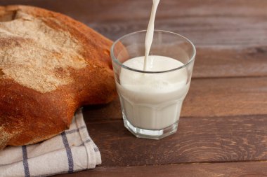 Tahta masada bir bardak sütle ekmek. Süt cama dökülüyor..