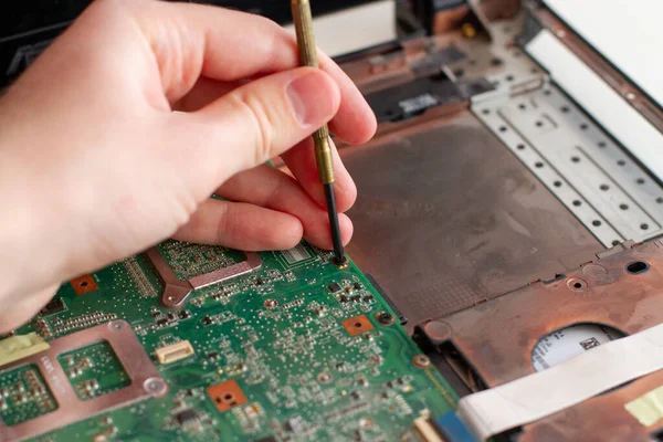 Computer repair technician working on motherboard with screwdriver.