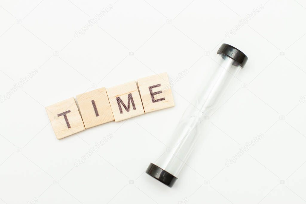 The concept of the passage of time. Inscription made of wooden blocks TIME and hourglass on a white background. Top view.