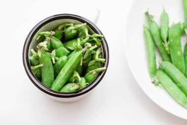 Beyaz metal bardakta ve tabakta yeşil bezelyeler. Seçici odak.