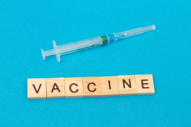 Kelime Aşıları ahşap küplerden ve mavi arka planda aşısı olan tıbbi şırıngadan yapılmış. Coronavirus. Covid 19 virüsü. Tıbbi bulaşıcı kavram
