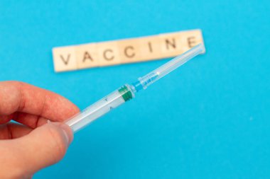 Elinde tıbbi şırınga ve mavi arka plandaki tahta küplerden yapılmış VACCINE. Coronavirus. Covid 19 virüsü. Tıbbi bulaşıcı kavram.