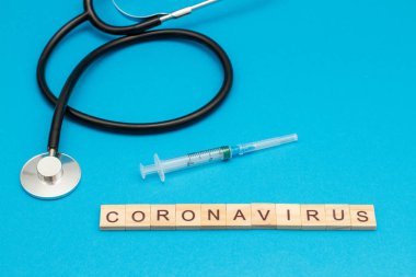 CORONAVIRUS kelime ahşap küplerden yapılmış stetoskop ve cerrahi şırınga ile mavi üzerine.