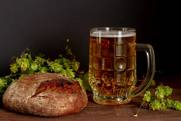 Glass of beer and dark bread on old wooden table and black background.