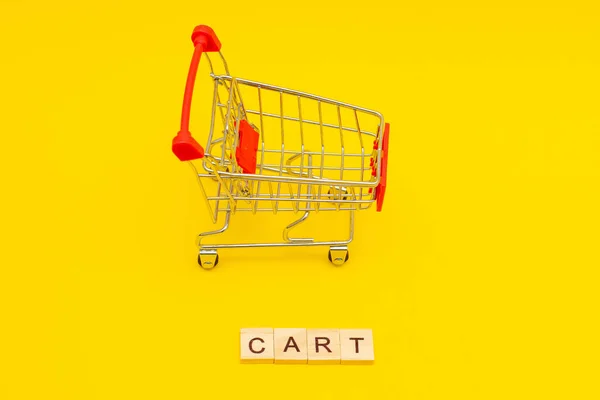 Palavra CARRINHO feito de cubos de madeira no fundo amarelo com brinquedos carrinho de compras — Fotografia de Stock