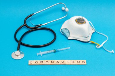 CORONAVIRUS kelime ahşap küplerden yapılmış solunum cihazı, stetoskop ve şırınga ile mavi üzerine.