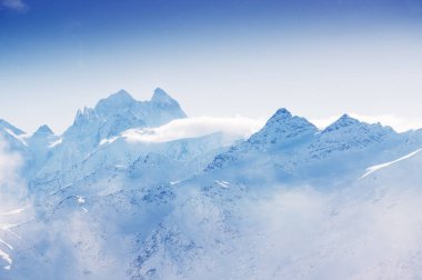 Karla kaplı dağ zirveleri bulutlu gün batımında. Güzel kış manzarası.