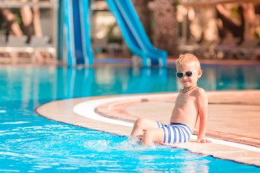 Sevimli küçük çocuk havuzu kenarında oturan güneş gözlüğü