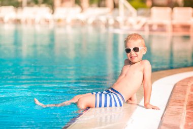 Sevimli küçük çocuk havuzu kenarında oturan güneş gözlüğü
