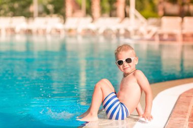 Sevimli küçük çocuk havuzu kenarında oturan güneş gözlüğü