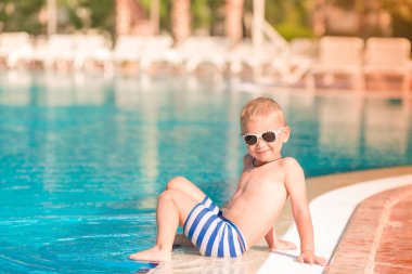 Sevimli küçük çocuk havuzu kenarında oturan güneş gözlüğü