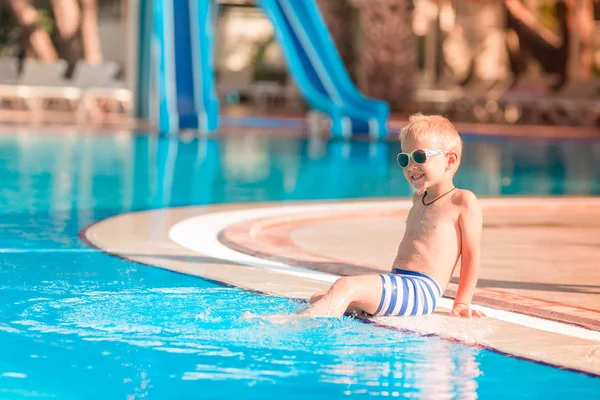 Sevimli küçük çocuk havuzu kenarında oturan güneş gözlüğü