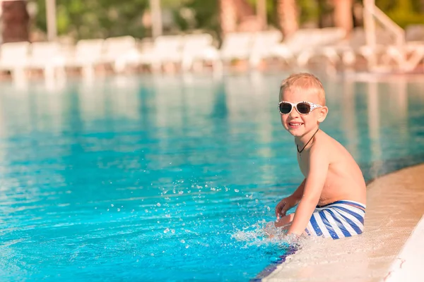 Sevimli küçük çocuk havuzu kenarında oturan güneş gözlüğü