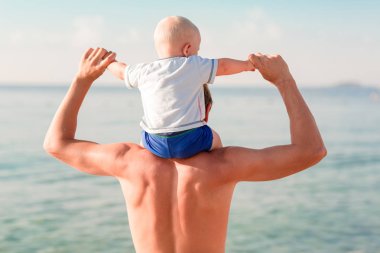 Mutlu bebek plajda denize bakarak babasının omuzlarında oturan