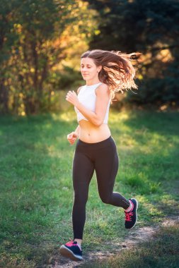 Güzel genç sportif kadın günbatımı ışık parkta koşu