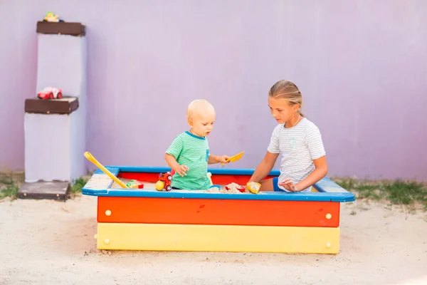 Lindo bebé jugando con su hermana en la caja de arena —  Fotos de Stock