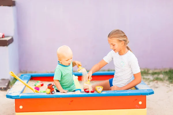 Lindo bebé jugando con su hermana en la caja de arena — Foto de Stock