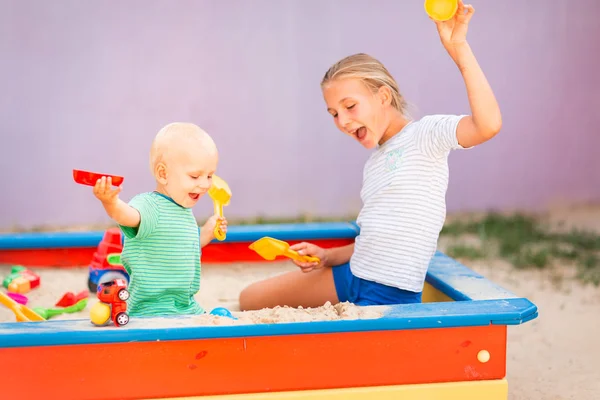 Lindo bebé jugando con su hermana en la caja de arena —  Fotos de Stock