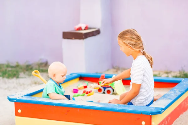 Lindo bebé jugando con su hermana en la caja de arena —  Fotos de Stock