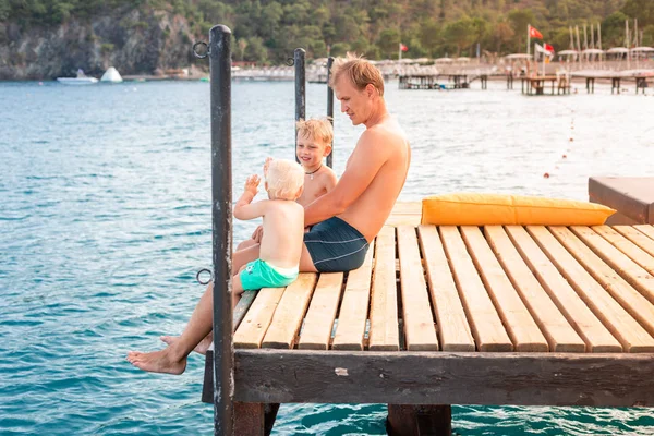 Vater und Söhne schwingen die Beine vom Holzsteg — Stockfoto