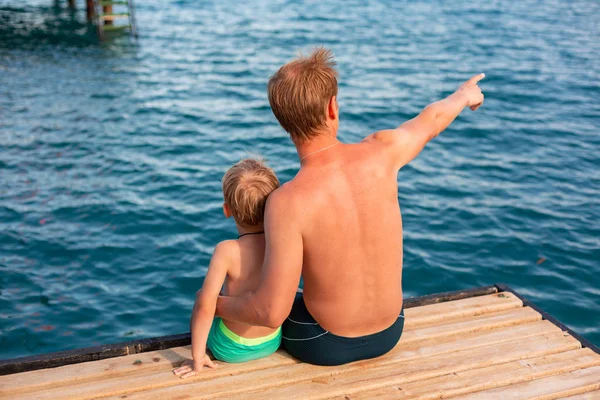 Padre e hijo balancean sus piernas desde el muelle de madera — Foto de Stock