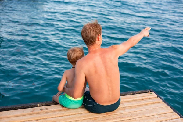 Padre e hijo balancean sus piernas desde el muelle de madera — Foto de Stock