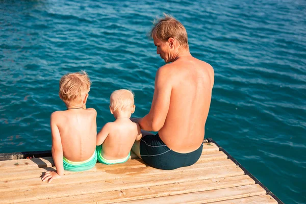 Vader en zonen slingeren hun benen van de houten pier — Stockfoto