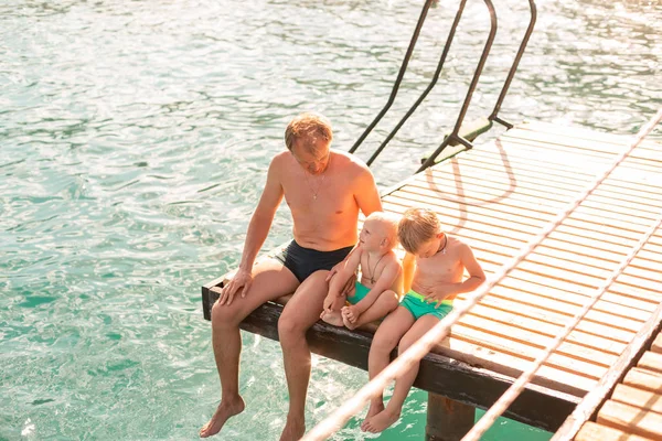 Baba ve oğulları ahşap iskeleden bacaklarını sallayarak — Stok fotoğraf