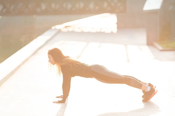 Mujer de fitness haciendo ejercicio de tablón durante el entrenamiento al aire libre en ambiente urbano —  Fotos de Stock