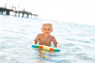 Mutlu çocuk deniz kenarındaki dalgalarda yüzme tahtasıyla oynuyor.
