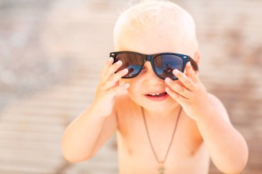 Kumsalda büyük güneş gözlükleriyle poz veren sevimli erkek bebek.