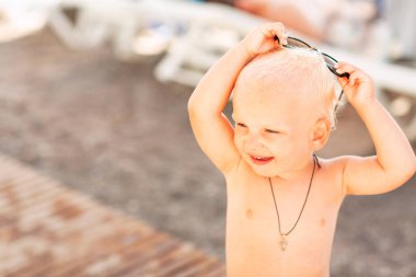 Kumsalda büyük güneş gözlükleriyle poz veren sevimli erkek bebek.