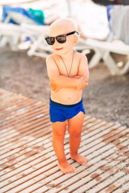 Kumsalda büyük güneş gözlükleriyle poz veren sevimli erkek bebek.