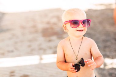 Kumsalda büyük güneş gözlükleriyle poz veren sevimli erkek bebek.