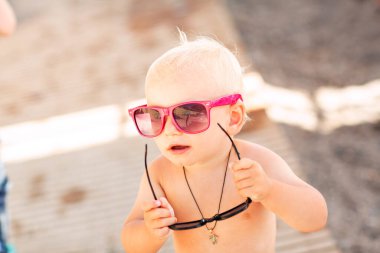 Kumsalda büyük güneş gözlükleriyle poz veren sevimli erkek bebek.