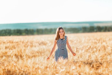 Mutlu genç güzel kız gün batımında altın buğday tarlasında koşuyor.