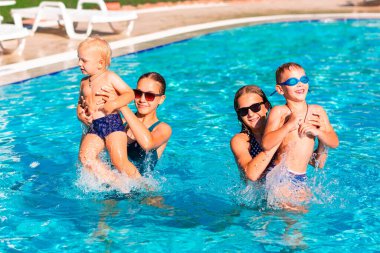 Mutlu çocuklar havuzda eğleniyor. Çocuklar yaz tatili boyunca açık deniz tatil beldesinde oynuyorlar. Tatildeki çocuklar için su ve su serpme eğlencesi.
