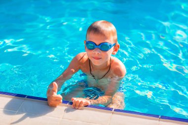 Yüzme havuzunda yüzen ve yüzen, gözlüklü şirin, mutlu küçük bir çocuk.
