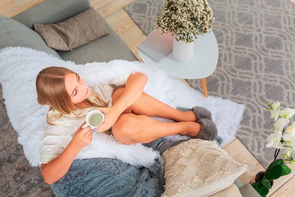年轻美丽的姑娘坐在沙发上 裹着舒适的毯子和一杯咖啡 — 图库照片