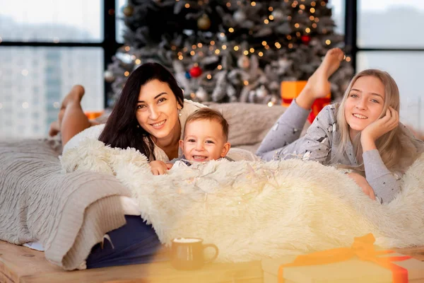 圣诞树旁快乐的家庭 早上妈妈和孩子们穿着睡衣在树旁玩乐 圣诞快乐及假期快乐的概念 — 图库照片